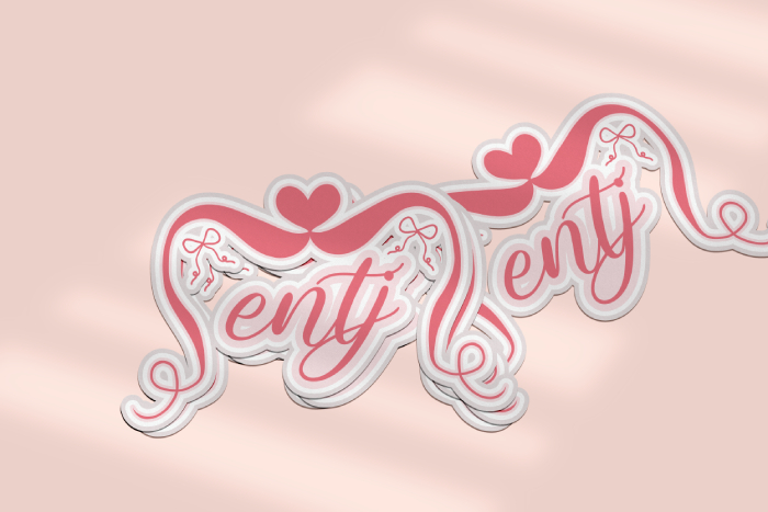 A mockup of an ENTJsticker showing a stack of three stickers in the foreground, with a single sticker cast off to the side behind them. The design is a pink coquette aesthetic with script lettering, a heart, and bows.