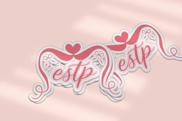 A mockup of an ESTP sticker showing a stack of three stickers in the foreground, with a single sticker cast off to the side behind them. The design is a pink coquette aesthetic with script lettering, a heart, and bows.