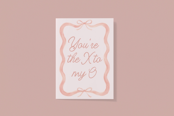 A peachy pink Galentine's card featuring a wavy ribbon border with bows and the text "You're the X to my O" in cursive.