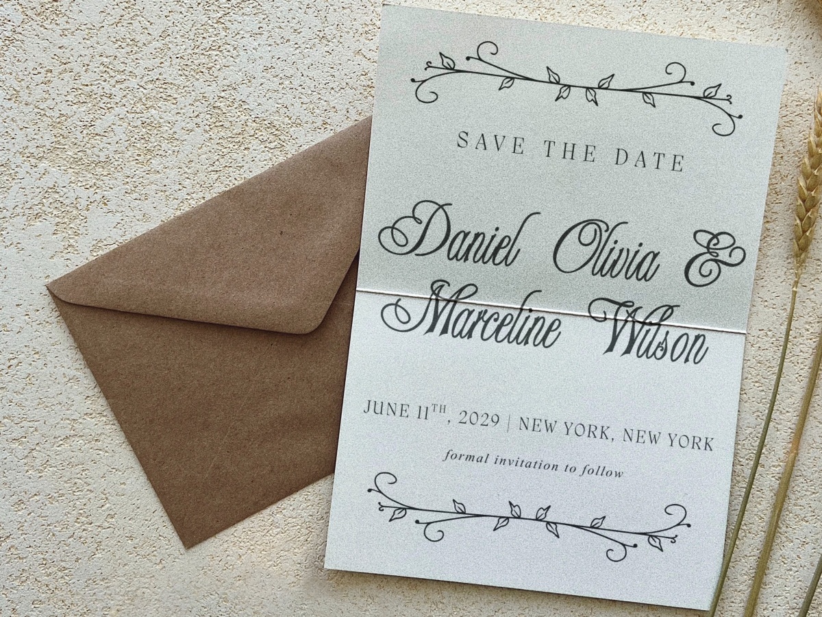 A wedding save-the-date card with a brown envelope, featuring decorative floral borders and elegant script text announcing a June 11, 2029 wedding in New York City.